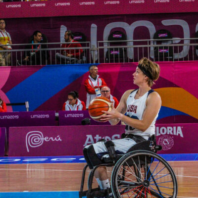 Abby Dunkin playing Wheelchair Basketball. It appears as though she is about to shoot the ball during a game. She is wearing a Team USA uniform.